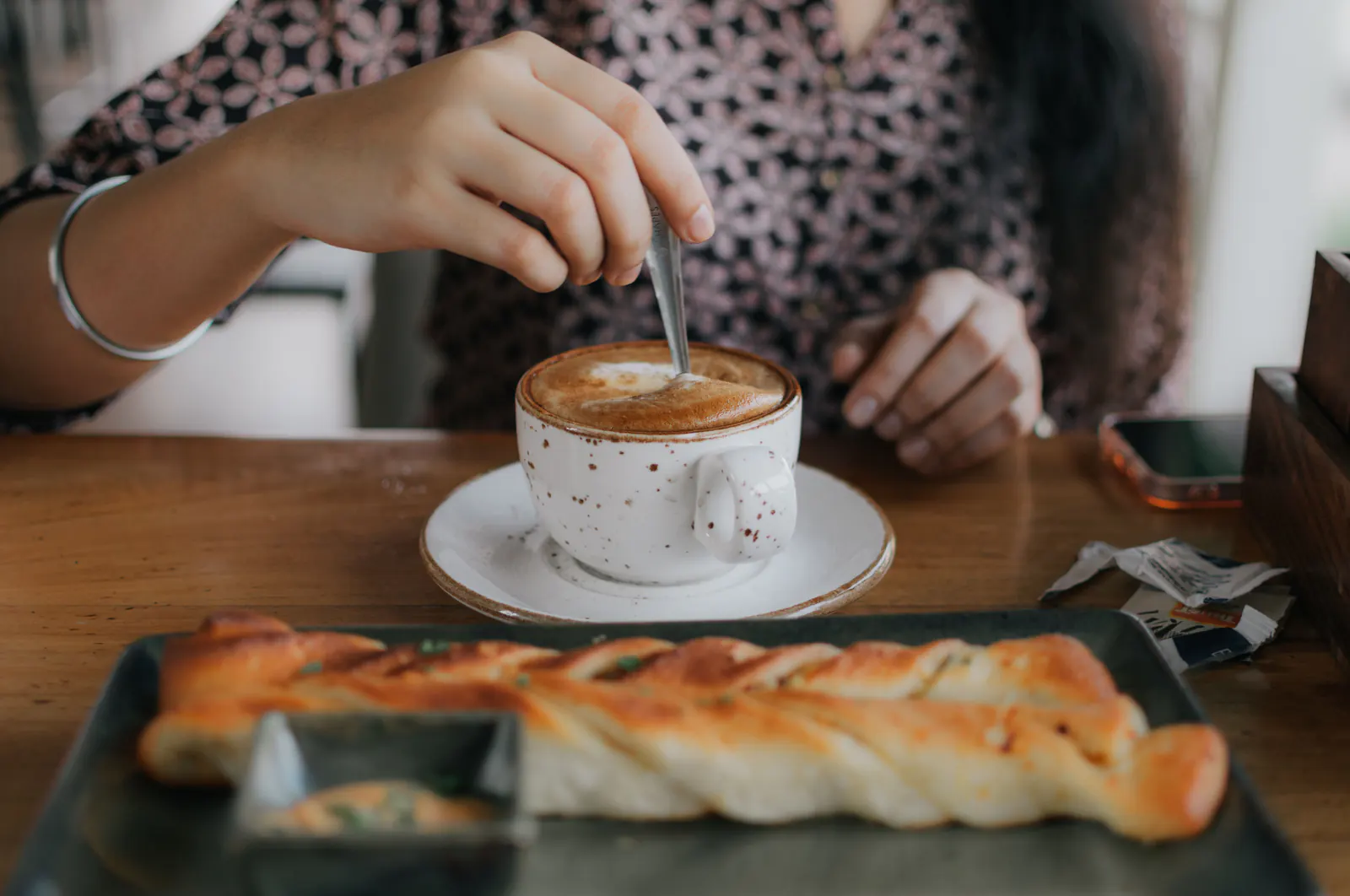 Cafe customer stirring a cup of coffee beside a pastry