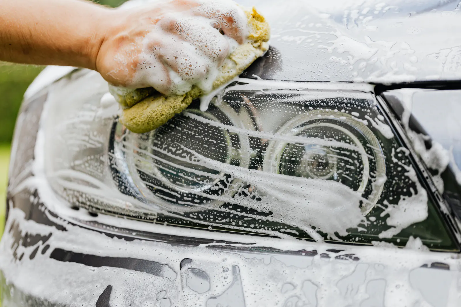 Car detailer washing a vehicle headlight by hand